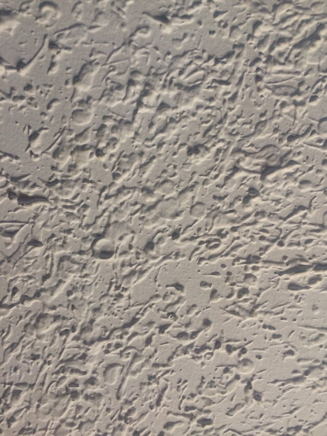A pale ceiling finished in a heavily stippled and swirled textured coating.