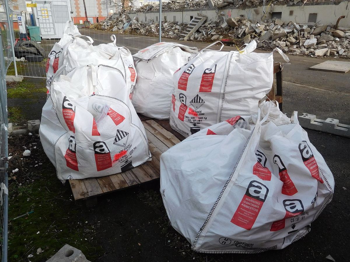 Five heavy-duty bulk bags on wooden pallets, each printed with a red and black WARNING CONTAINS ASBESTOS label and the UN hazard code.