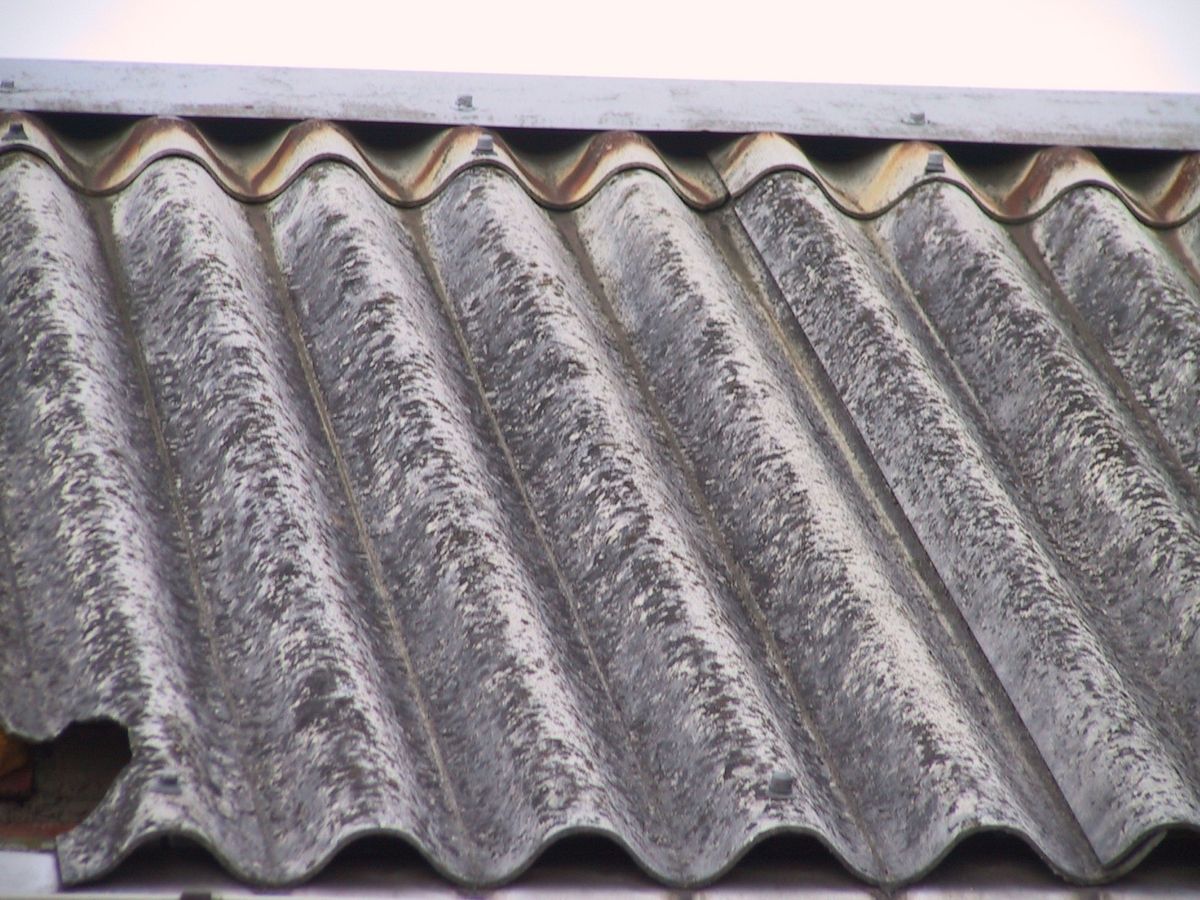 Weathered grey corrugated cement roof sheets in close-up, with a triangular section broken away from the bottom corner of one sheet.