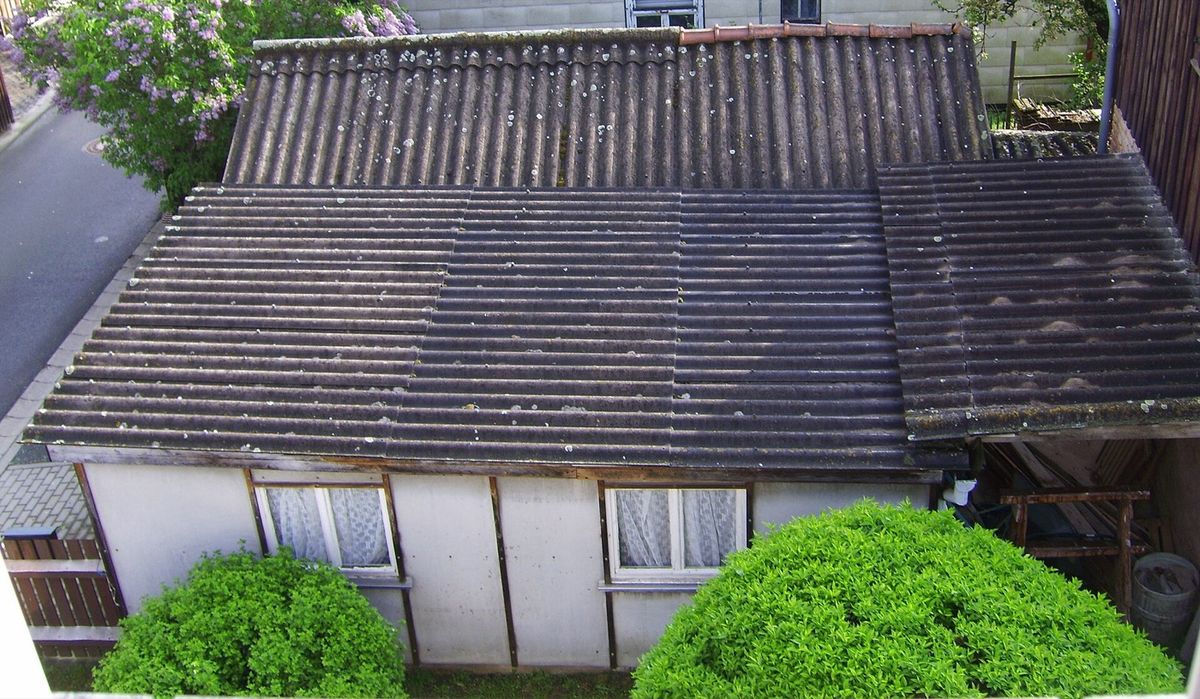 A detached garage with a weathered corrugated asbestos cement roof and flat asbestos cement wall panels.